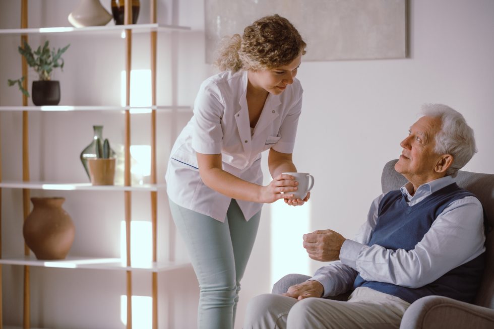 Opiekunka podaje seniorowi filiżankę herbaty